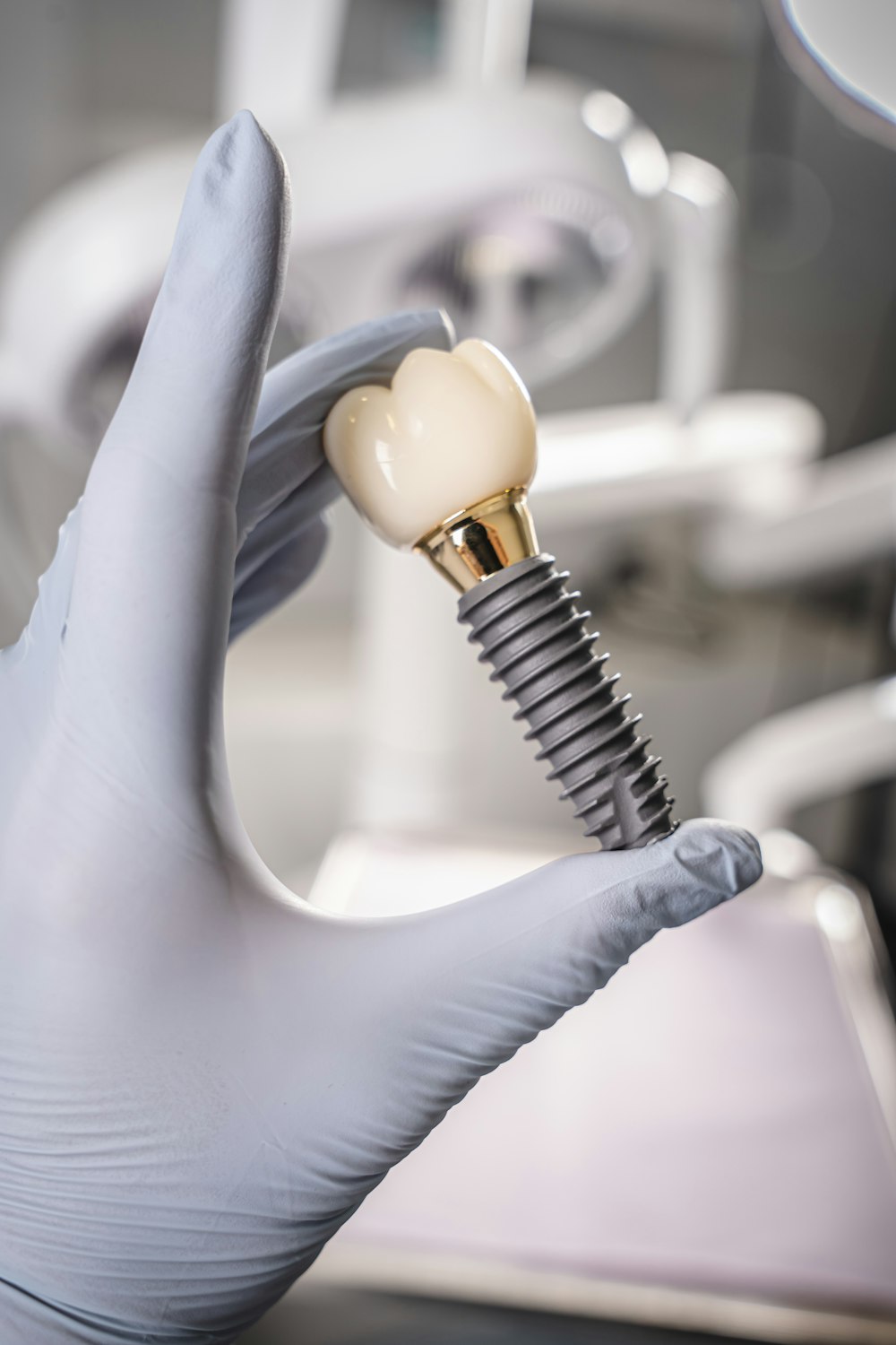 Gloved hand holding a dental implant and crown